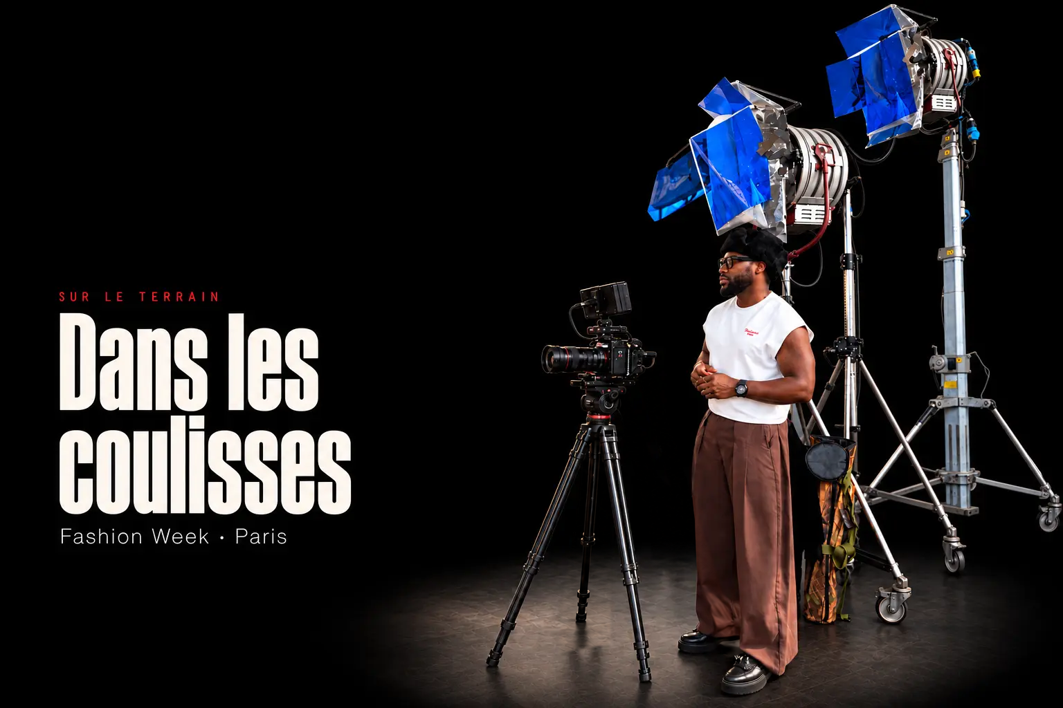 Charles en pied sur un tournage, avec sa caméra sur trépied et deux grands projecteurs, sur fond noir.